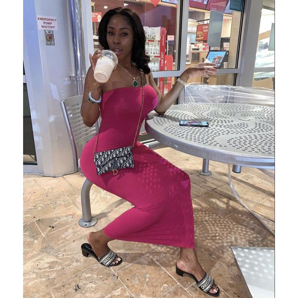 Woman in a form-fitting pink dress sitting outdoors, sipping a beverage, wearing sandals and a stylish crossbody bag.